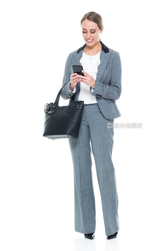 向下看/一个人/全身/正面视图20-29岁的成年美丽的白人女性/年轻女性商人/商人站着穿着西装拿着手机/钱包/使用智能手机/短信